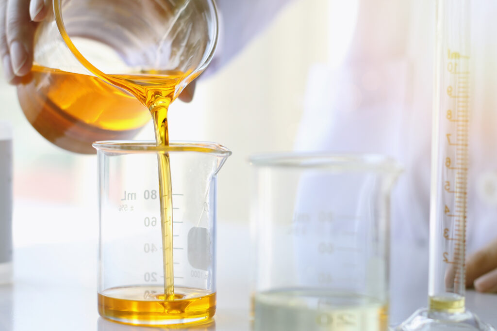 Pouring botanical oil into glass beaker for oil-based skincare formulation