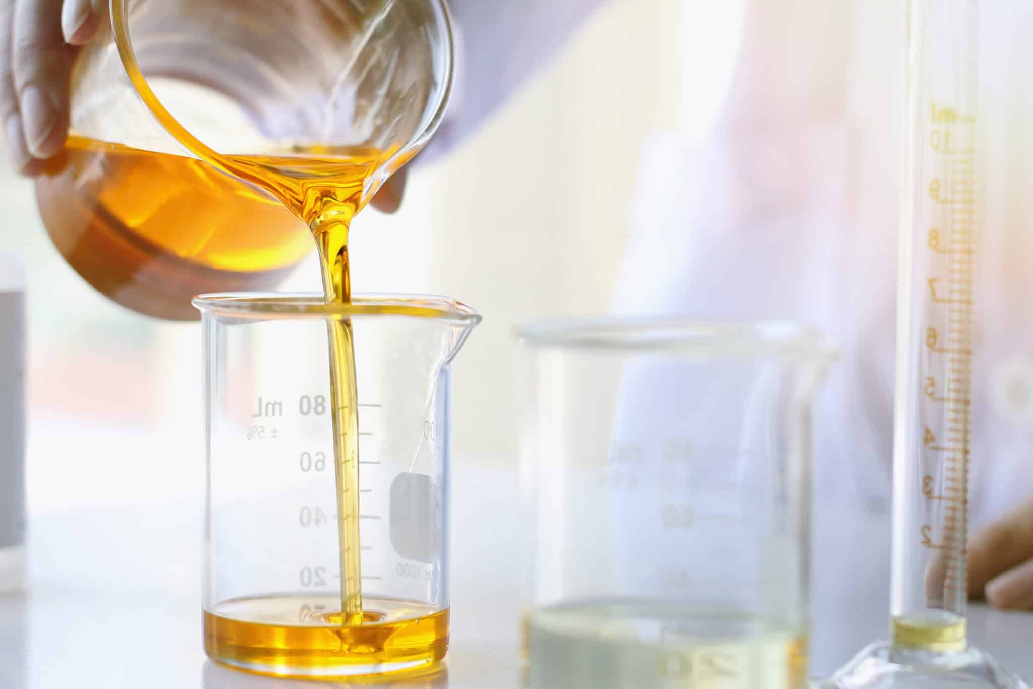 Pouring botanical oil into glass beaker for oil-based skincare formulation