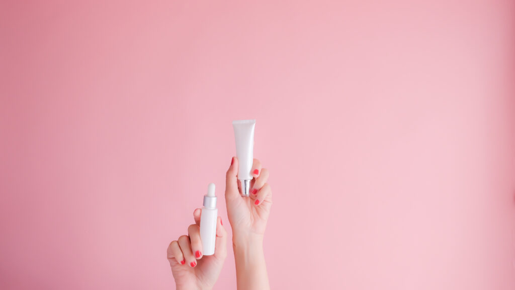 Hand holding a facial oil bottle on pink background – concept image for facial oil vs moisturizer blog