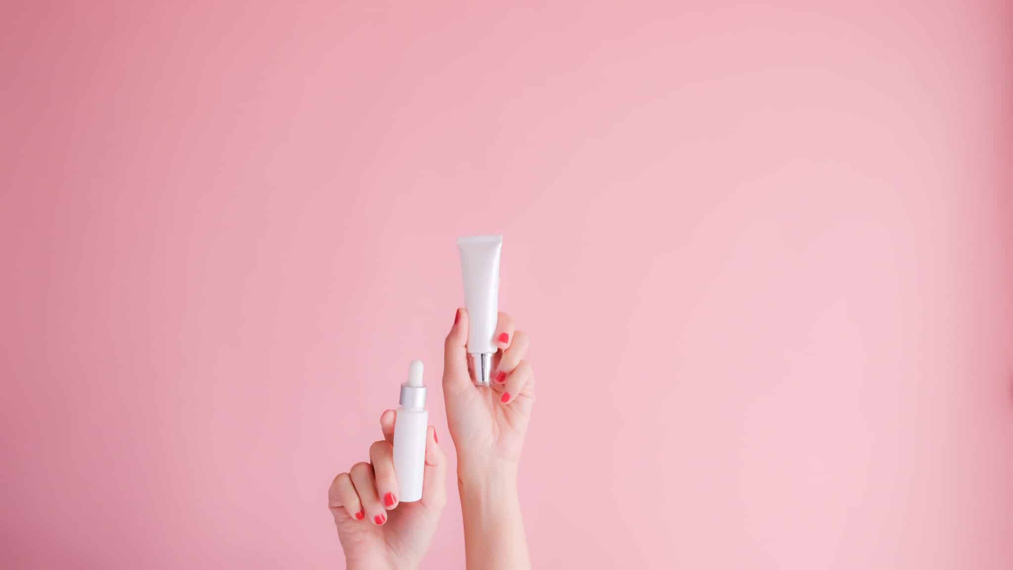 Hand holding a facial oil bottle on pink background – concept image for facial oil vs moisturizer blog