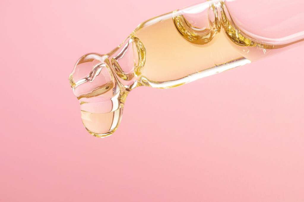 Facial oil texture dripping on pink background, illustrating occlusive skincare action