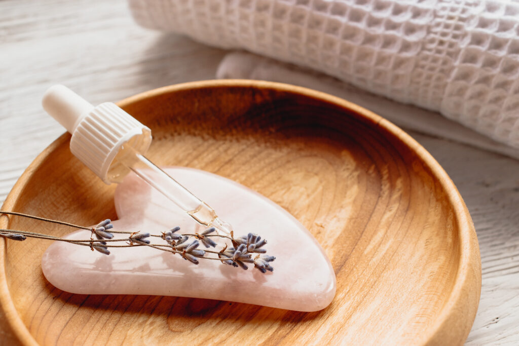 Facial oil dropper on rose quartz Gua Sha stone with lavender, placed in a wooden bowl