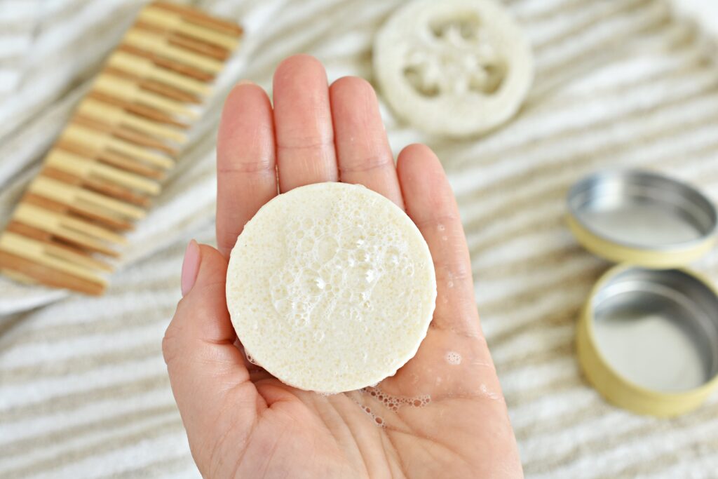 woman holding a solid shampoo bar with foam, symbolizing gentle and eco-friendly haircare.