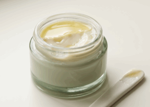 Open glass jar containing a broken oil-in-water cream emulsion with separated oil layer on top, illustrating cosmetic formulation failure after 24 hours